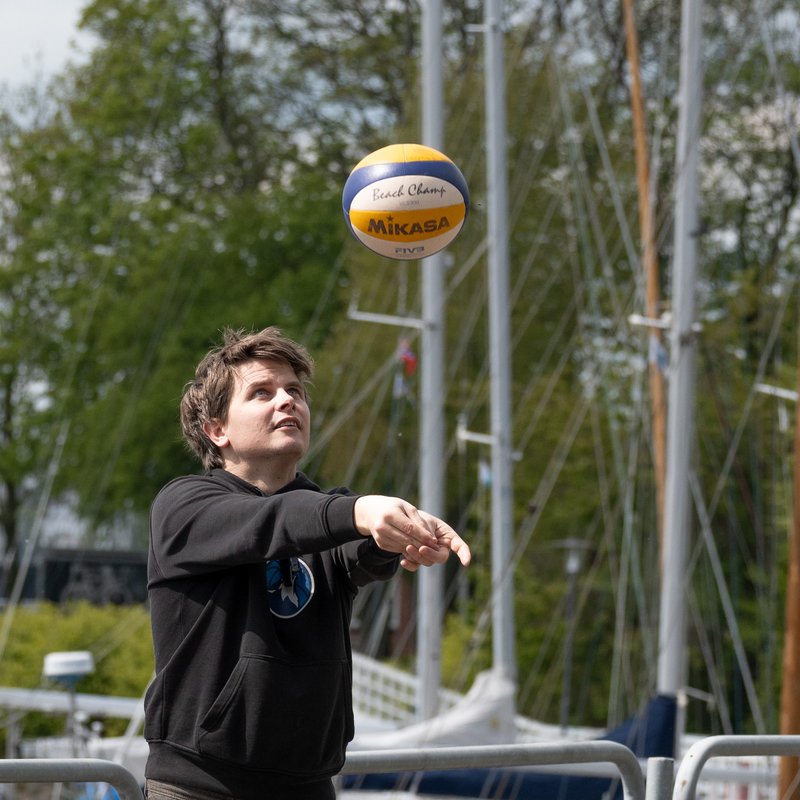 ein Mann spielt mit einem Beach-Volleyball am Steg hinter der Schwentine Mensa in Kiel 