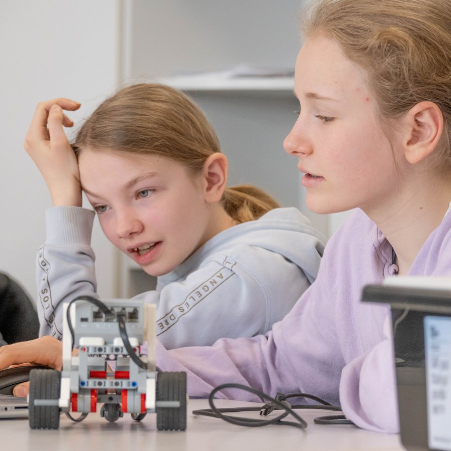 Zwei Mädchen vor einem Laptop. Neben ihnen steht ein LEGO-Roboter.